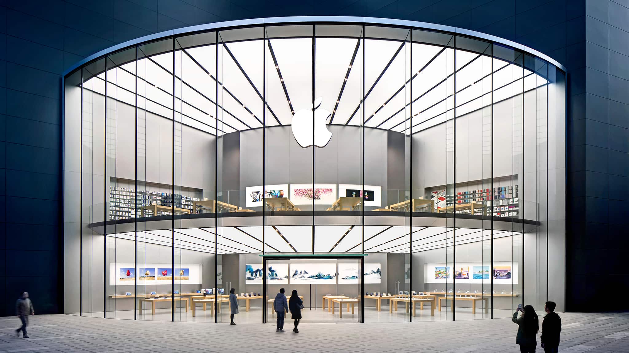 Exterior view of the 2 storey high Apple Xinjiekou, featuring 14 meter tall curved monolithic glass panels arranged around the corner of the mall creating a fan shaped footprint of the store.